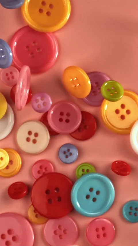 Multi-colored sewing buttons fall on a red table. Filmed on a high-speed camera Stock Footage 335379390