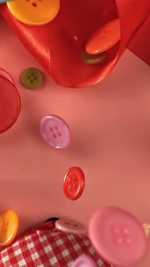Multi-colored sewing buttons fall on a red table. Filmed on a high-speed camera Stock Footage 335379536