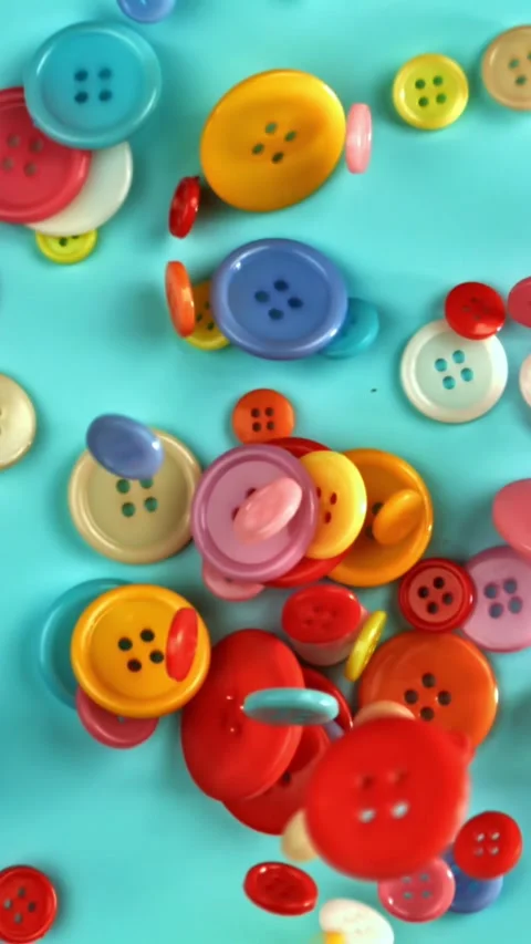 Multi-colored sewing buttons fall on the table. Filmed on a high-speed camera at Stock Footage 335379631