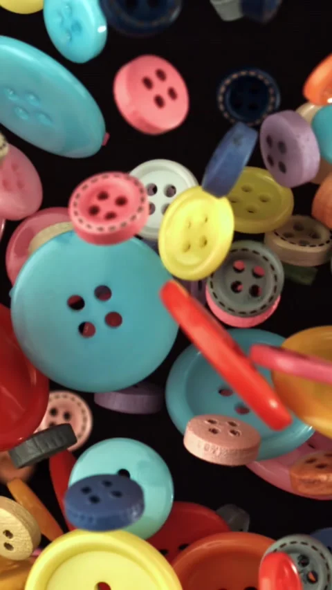 Multi-colored sewing buttons fly on a black background. Filmed on a high-speed Stock Footage 335377971