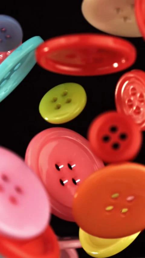 Multi-colored sewing buttons fly on a black background. Filmed on a high-speed Stock Footage 335379561