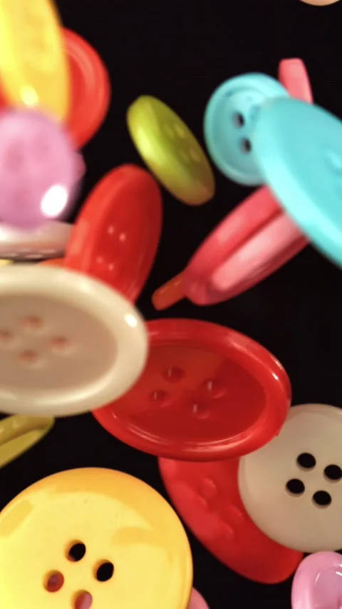 Multi-colored sewing buttons fly on a black background. Filmed on a high-speed Stock Footage 335380432