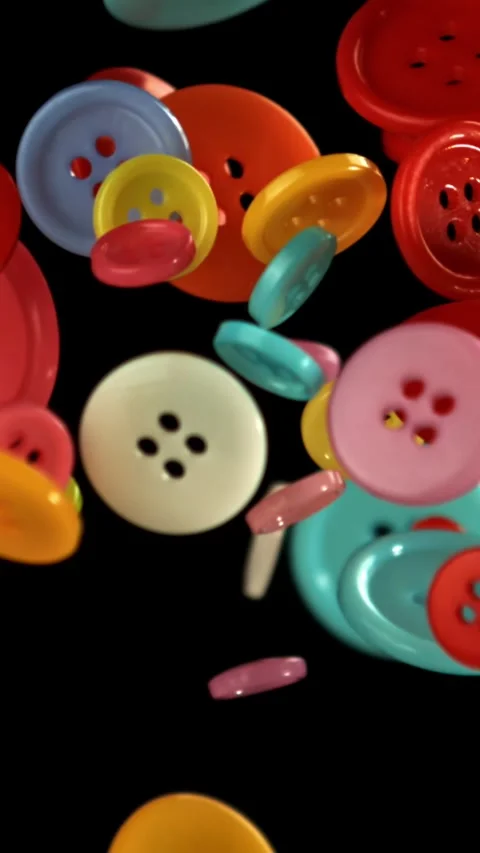 Multi-colored sewing buttons fly on a black background. Filmed on a high-speed Stock Footage 335381497