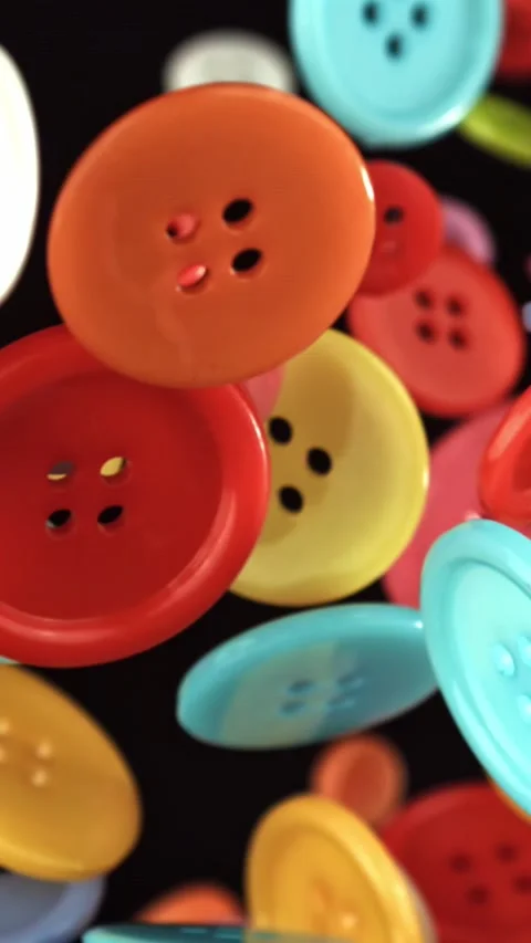 Multi-colored sewing buttons fly on a black background. Filmed on a high-speed Stock Footage 335381804