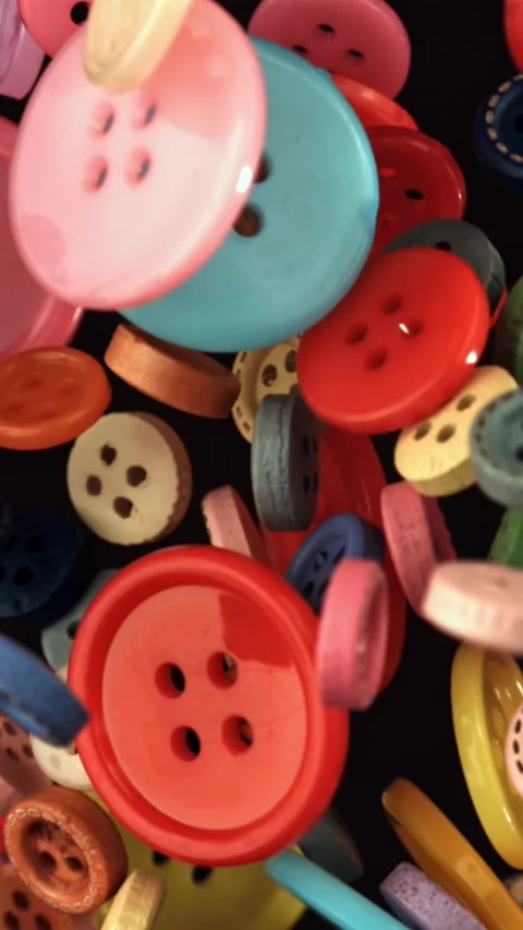 Multi-colored sewing buttons fly on a black background. Filmed on a high-speed Stock Footage 335381867