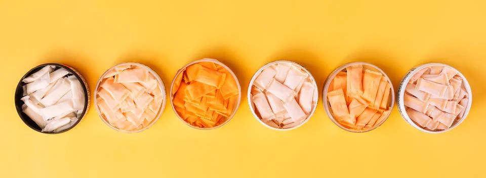 Multi-colored snus sachets with different flavors are placed in jars on a yellow Stock Photos