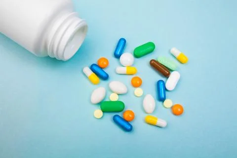 Multi-colored tablets and capsules, white bottle for tablets, pharmaceutical  Stock Photos