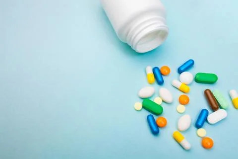 Multi-colored tablets and capsules, white bottle for tablets, pharmaceutical  Stock Photos