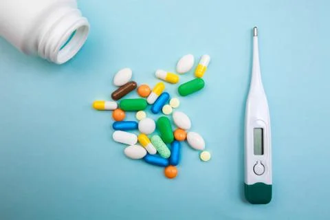 Multi-colored tablets and capsules, thermometer and on a blue background, con Stock Photos