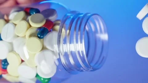 Multi-colored tablets are pouring out of the neck of a plastic pill package onto Stock Footage 261185702