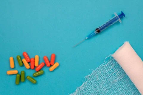 Multi-colored tablets are scattered on the table, a syringe, a needle, a bandage Stock Photos