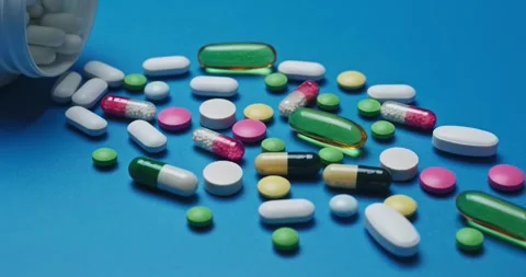 Multi-colored tablets spilling out of open bottle on to surface Stock Footage 303240481