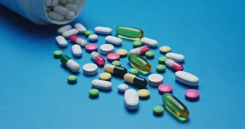 Multi-colored tablets spilling out of open bottle on to surface Vídeos de archivo 303240493