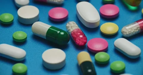 Multi-colored tablets spilling out of open bottle on to surface 스톡 동영상 303241162