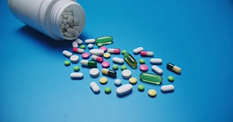 Multi-colored tablets spilling out of open bottle on to surface 動画素材 303241427