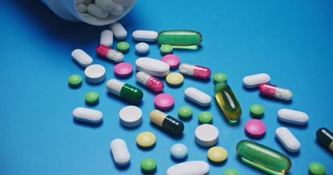 Multi-colored tablets spilling out of open bottle on to surface Vídeos de archivo 303241723