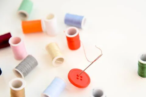 Multi colored thread spools, needle and red button Stock Photos