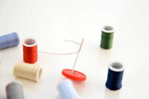 Multi colored thread spools, needle and red button Stock Photos