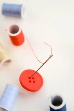 Multi colored thread spools, needle and red button Foto stock