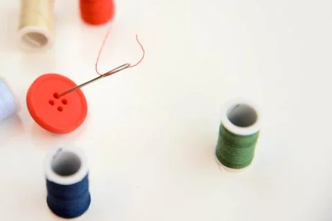 Multi colored thread spools, needle and red button Stock Photos