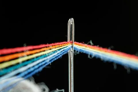Multi-colored threads for sewing in the form of a rainbow pass through an a.. Stock Photos
