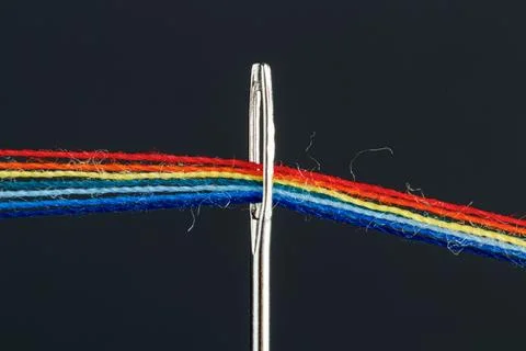 Multi-colored threads for sewing in the form of a rainbow pass through an a.. Stock Photos