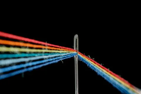 Multi-colored threads for sewing in the form of a rainbow pass through an a.. Stock Photos