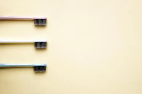 Multi-colored toothbrushes on a yellow background with space for text, flat l Stock Photos