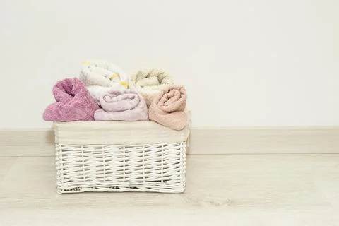 Multi-colored towels rolled into rolls in a white wicker basket on the floor Stock Photos