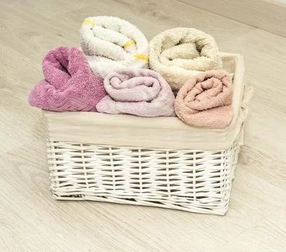 Multi-colored towels rolled into rolls in a white wicker basket on the floor Stock Photos