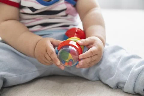 Multi-colored toy in the hands of a child, who sits on the bed Stock Photos