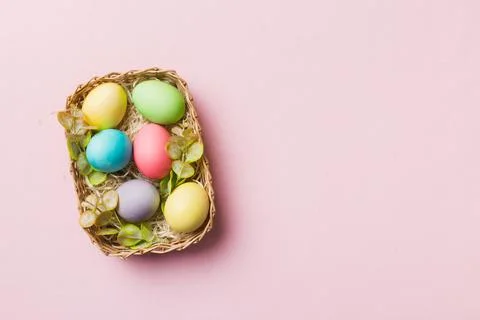 Multi colors Easter eggs in the woven basket on colored background . Pastel c Foto stock