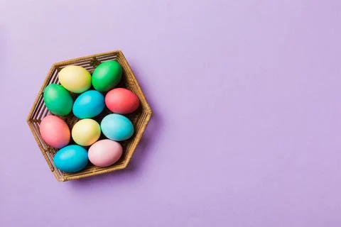 Multi colors Easter eggs in the woven basket on colored background . Pastel c Foto stock