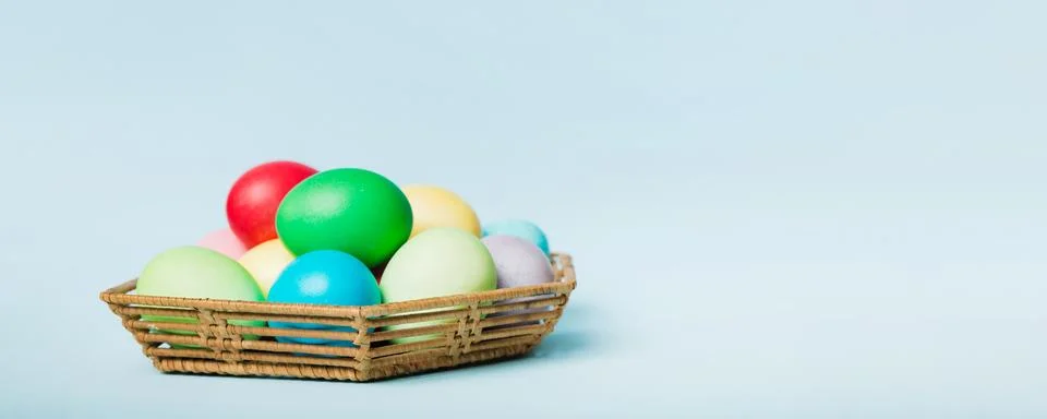 Multi colors Easter eggs in the woven basket on colored background . Pastel.. 库存照片