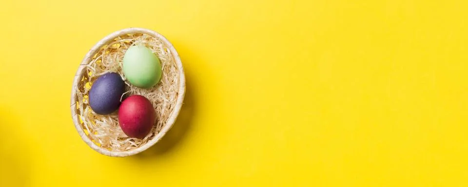 Multi colors Easter eggs in the woven basket on colored background . Pastel c Stock Photos