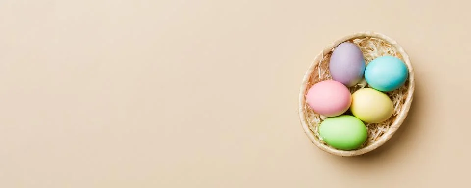 Multi colors Easter eggs in the woven basket on colored background . Pastel c Foto stock