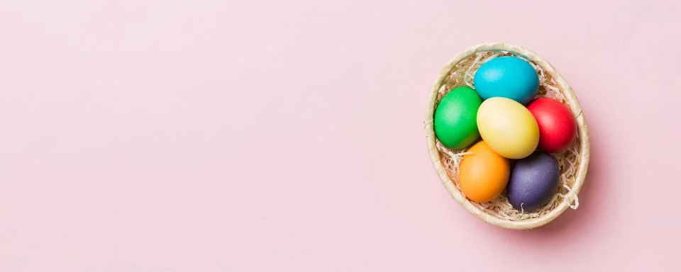 Multi colors Easter eggs in the woven basket on colored background . Pastel.. Stock Photos