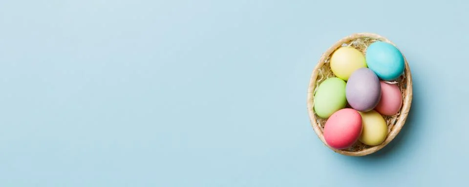Multi colors Easter eggs in the woven basket on colored background . Pastel.. Stock Photos