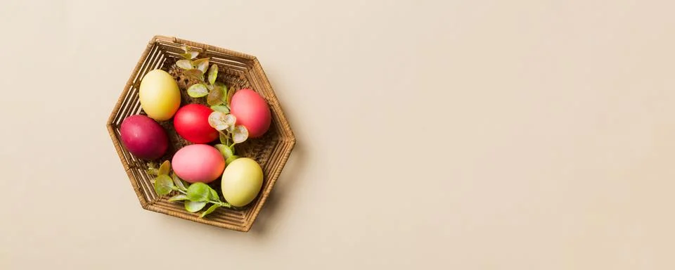 Multi colors Easter eggs in the woven basket on colored background . Pastel.. Stock Photos