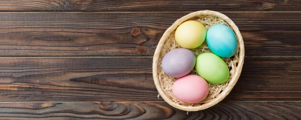 Multi colors Easter eggs in the woven basket on colored background . Pastel c Stock Photos
