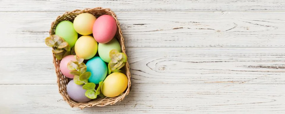 Multi colors Easter eggs in the woven basket on colored background . Pastel.. Stock Photos