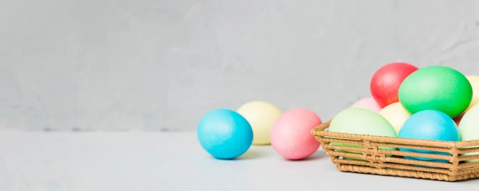 Multi colors Easter eggs in the woven basket on colored background . Pastel.. Stock Photos