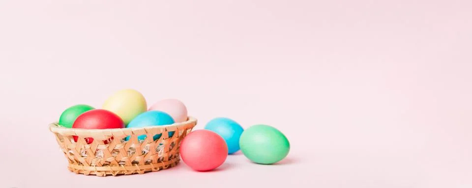 Multi colors Easter eggs in the woven basket on colored background . Pastel.. Stock Photos
