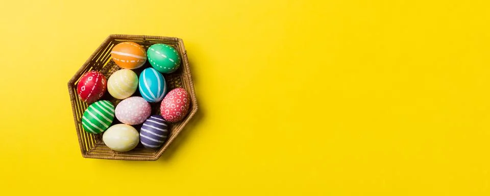 Multi colors Easter eggs in the woven basket on colored background . Pastel.. Stock Photos