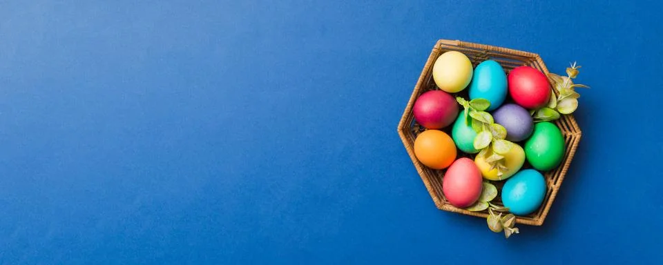 Multi colors Easter eggs in the woven basket on colored background . Pastel.. Stock Photos