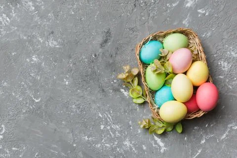 Multi colors Easter eggs in the woven basket on colored background . Pastel.. Stock Photos