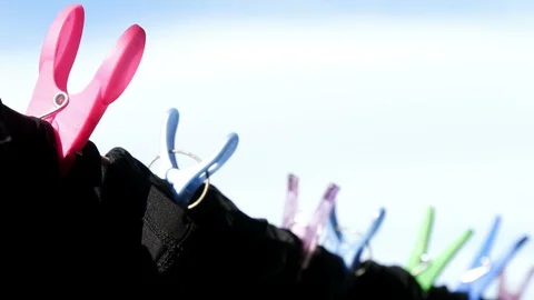 Multi Coloured close pegs holding all black garments on line, narrow depth field 動画素材 128703856