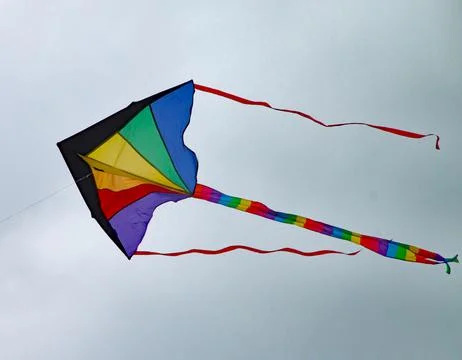 Multi coloured kite with a long tail and two streamers sours high in the sky Stock Photos