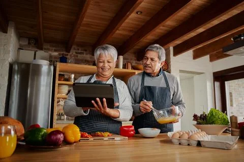 Multi-cultural elderly couple using tablet to research recipe in modern kitchen Stock Photos