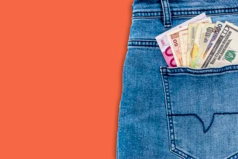 Multi currency banknotes in back pocket of blue jeans on orange colour backgr 库存照片